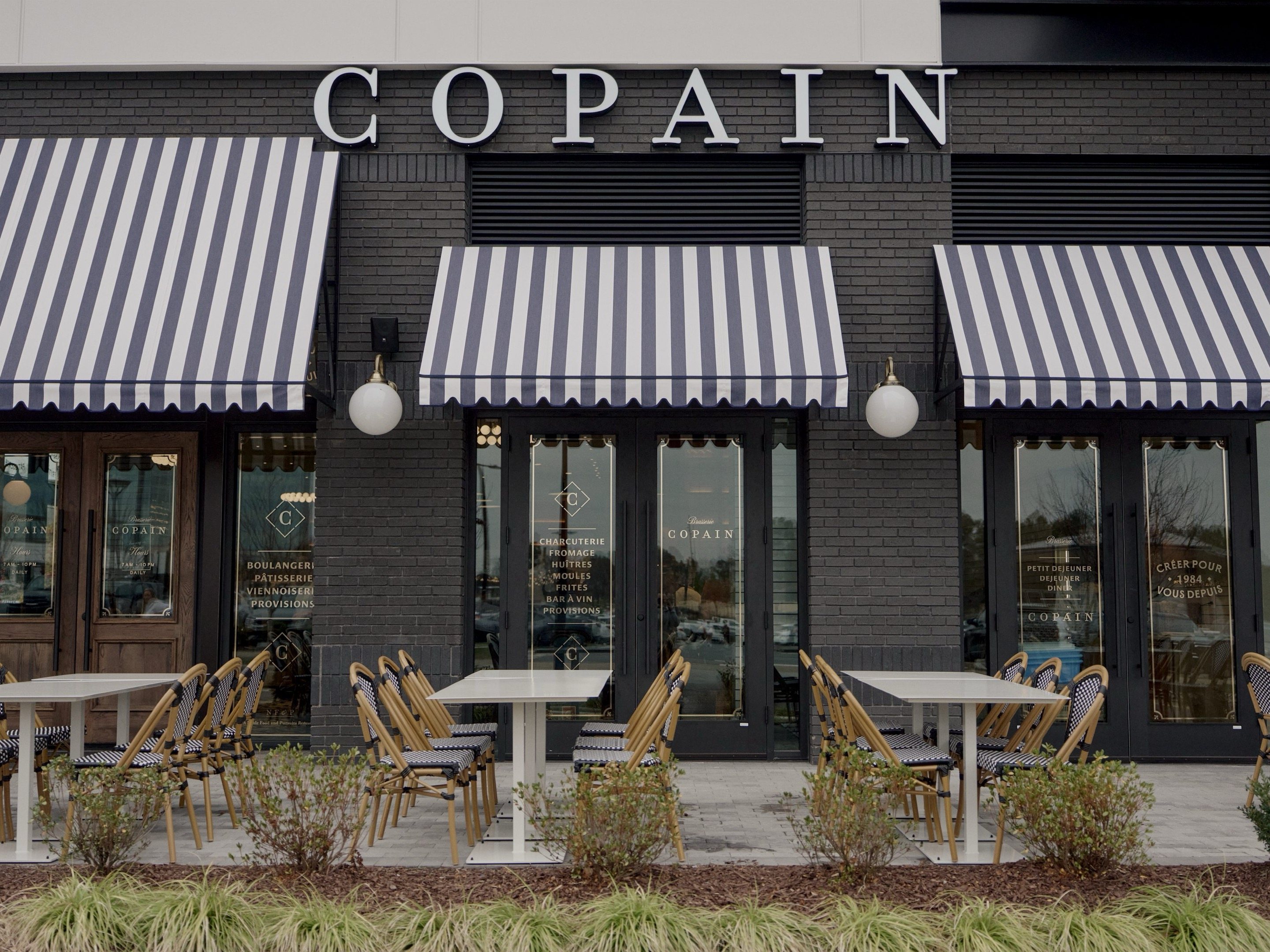 Ballantyne — dark brick facade with COPAIN signage and navy striped awnings and outdoor patio