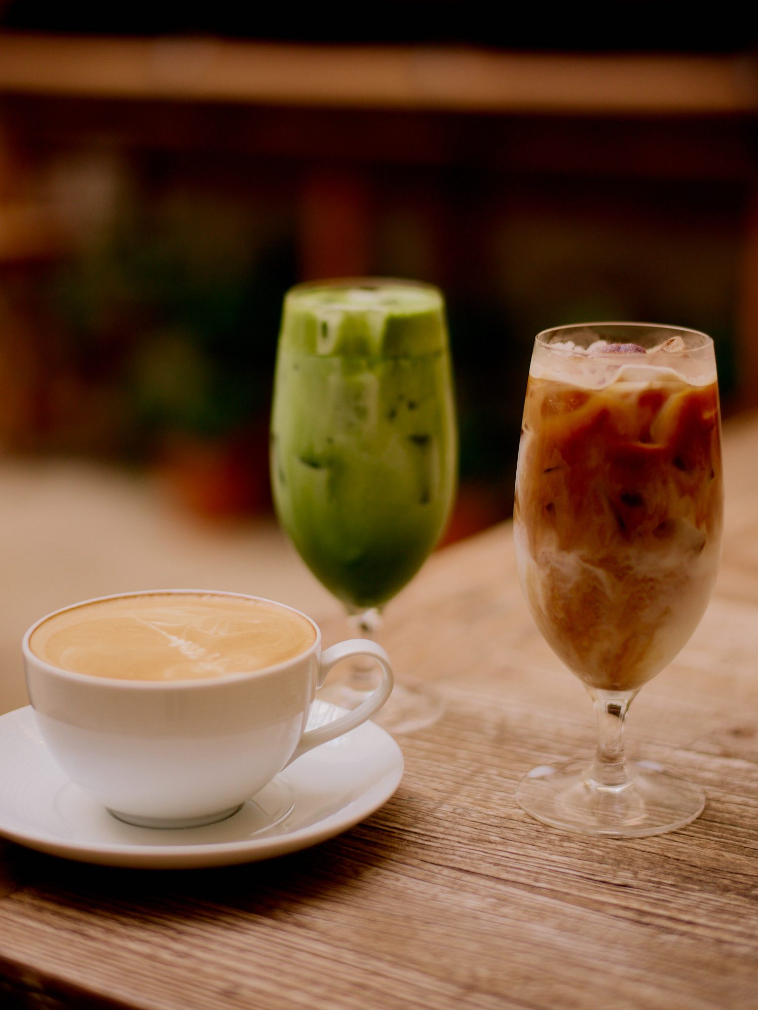 Café au lait, iced matcha, and iced coffee arranged on a wooden table