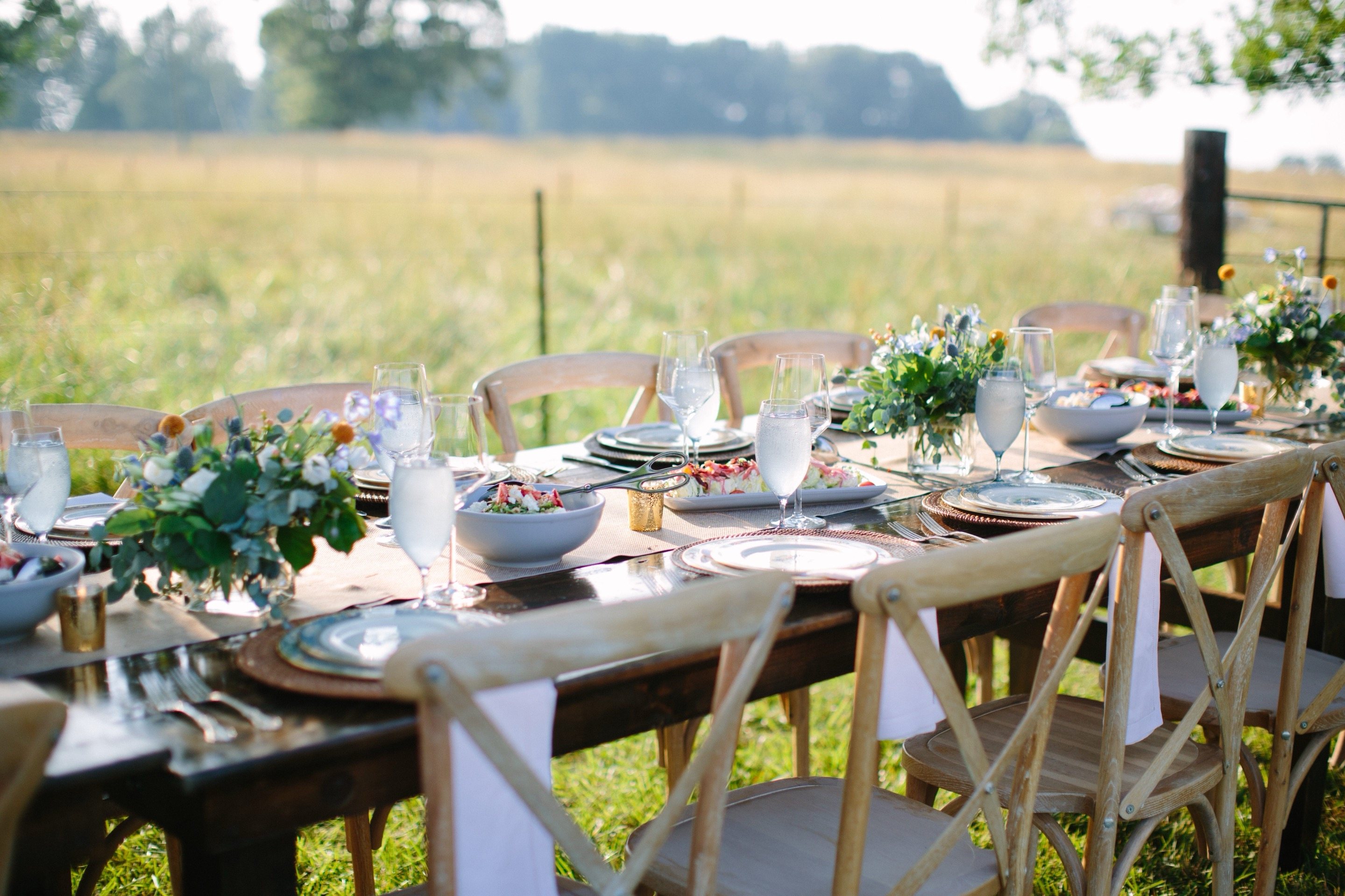 Elegant outdoor farm table catering setup with florals and full place settings in a golden field