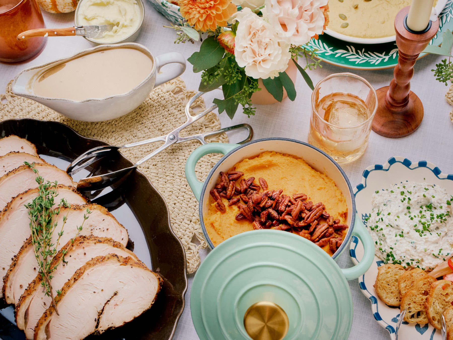 A styled Thanksgiving table with turkey, sweet potato casserole, candles, and autumn florals